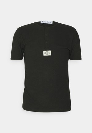Musta, lyhythihainen ribbineulos henley-paita, jossa on kolme nappia ja valkoinen suorakulmainen logolaatta rinnassa.