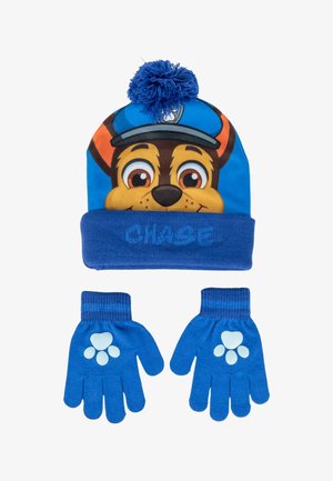 Bonnet tricoté bleu avec un visage de personnage et un pompon sur le dessus, associé à des gants bleus assortis présentant des motifs de empreintes de pattes sur les paumes.