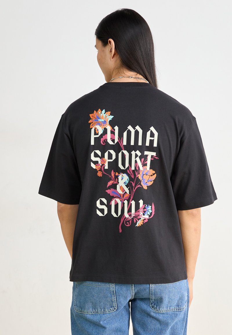Svart bomull t-shirt med stora blommönster i livliga färger och kraftfull text som säger "PUMA SPORT & SOUL" på baksidan.