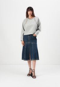Grå genser med utsmykket halslinning, sammen med en mørk denim midi-skjørt med en frontslitt og frynset kant. Svart stroppehæler.