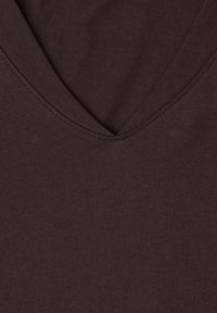 Mørkebrun stof med dyb V-udskæring og synlige syninger langs kanten, der viser en glat tekstur og jævnt væv.