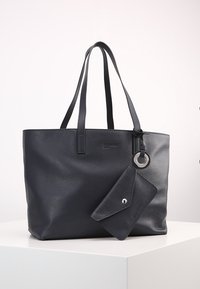 Sac cabas en cuir noir avec deux poignées et une pochette attachée de style enveloppe, posé sur une surface blanche avec un fond uni.