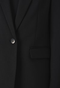 Black tailored blazer featuring a single button closure, notched lapels, and a front pocket with a smooth, textured fabric finish.