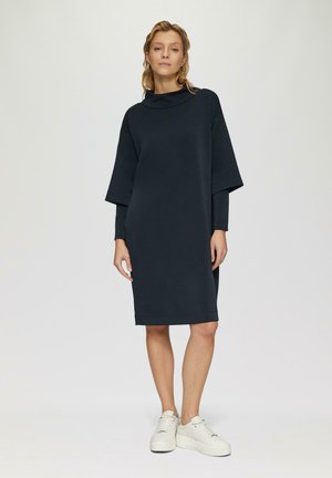 Námornícky oversized šaty s vysokým golierom a rukávmi v tvare netopiera, vyrobené z jemnej tkaniny. Nosené s bielymi platformovými teniskami.
