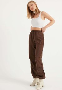 Braune, locker sitzende Hosen aus einem glatten Material, mit einem elastischen Bund und seitlichen Taschen. Kombiniert mit einem weißen gerippten Crop-Top und hellen Stiefeln.