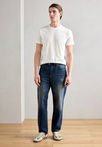 Hvid bomulds t-shirt, blå denim jeans med en falmet tekstur og beige sneakers med grønne striber. Simpelt design og afslappet pasform.