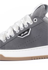 Gray suede sneaker with white laces and branding, featuring a white midsole and brown rubber outsole. Perforated detailing on the side.