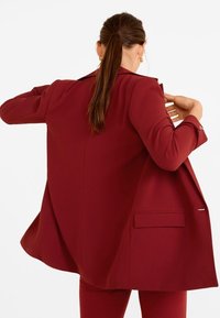 Blazer bordeaux au design ajusté, à manches longues et avec une poche sur le côté ; texture lisse et silhouette structurée.