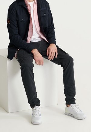 Pantalones casuales negros con un corte recto, combinados con una chaqueta azul marino y una camisa a cuadros rosa, complementados con zapatillas deportivas blancas.