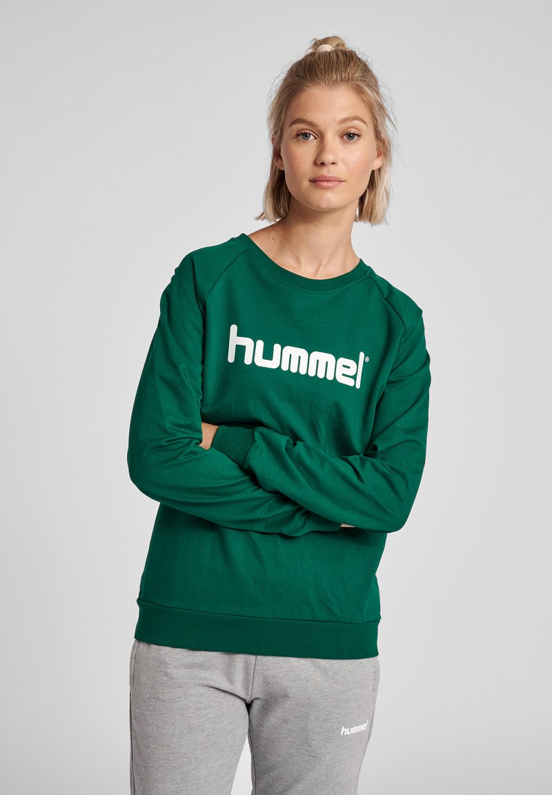 Felpa verde in cotone con scollo a U, caratterizzata da un logo bianco "hummel" sulla parte anteriore. Maniche e fondo a costine.