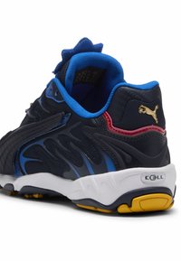 Laivansiniset ja mustat urheilukengät sinisillä korostuksilla, teksturoitu verkkomateriaali ylhäällä, valkoinen välikerros keltaisella ulkopohjalla, jossa on kultainen logo yksityiskohtana.