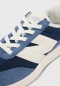 Baskets bleues avec un mélange de daim texturé et de matériaux en mesh, lacets blancs et un logo blanc bien en vue.