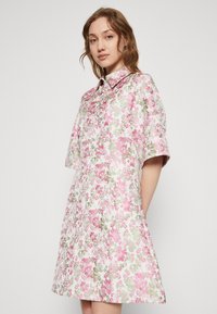 Rosa Blumenkleid mit kurzen Ärmeln, kragenförmigem Ausschnitt, aus leichtem Stoff, mit einem lebhaften Blumenmuster in Rosa und Grün.