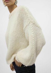 Pull en tricot épais de couleur blanc cassé avec une surface texturée, doté d'une coupe ample, de manches raglan et de surpiqûres décoratives sur les côtés.