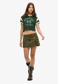 Groen katoenen cropped T-shirt met witte mouwen en opdruk "SUPERDRY 48 CALIFORNIA"; olijfgroene cargorok met zakken en knoop.