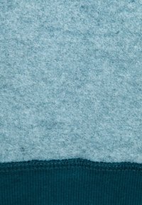 Tessuto di feltro azzurro chiaro con una superficie texture, che si trasforma in una banda rigata color teal scuro nella parte inferiore, caratterizzata da una cucitura liscia.