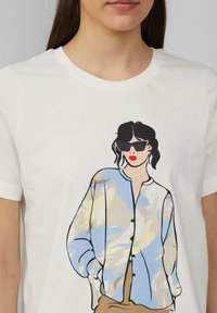 T-shirt blanc avec une illustration d'une femme portant des lunettes de soleil, vêtue d'une chemise à motifs bleus et beiges, avec des détails contourés en noir.