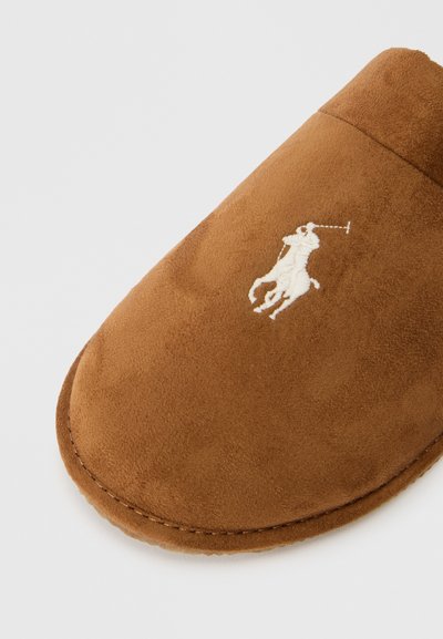Chinelo de camurça castanho com bico arredondado, apresentando um logótipo bordado em branco de um cavalo e cavaleiro na parte superior. Textura suave, costura detalhada.