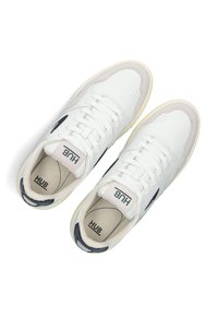 Witte leren sneakers met een beige suède acccent, platte veters en een marineblauw logo aan de zijkant. Geprofileerde zolen en gevoerde binnenkant.