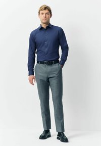 Tengerészeti hosszú ujjú ing gombos záródással, világosszürke kockás nadrággal és fekete elegáns cipővel párosítva. Egyszerű, testhezálló fazon.