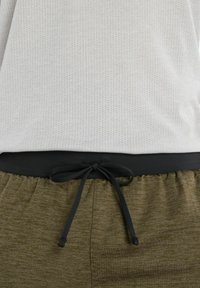 Vaaleanharmaa lyhythihainen paita, jossa on rei'itetty rakenne, tumman joustavan vyötärönauhan yläpuolella, yhdistettynä oliivinvihreisiin, teksturoituihin naruhousuihin.