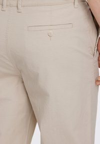 Beiga bomullsbyxor med en strukturerad yta, med en bakficka som har stängning med en enda knapp.