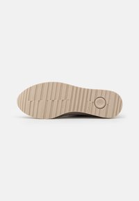Beige rubber shoe sole with a textured, ridged pattern. Features a circular branding detail. Smooth finish with a flat, wide profile.
