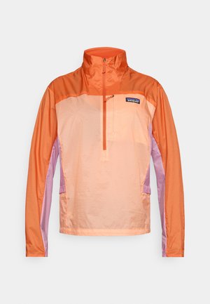 Patagonijos megztinis-oranžinės ir šviesiai violetinės spalvos. Yra aukštas apykaklė, pusiau užtrauktukas priekyje ir tekstūruotas audinys su raštuotomis sekcijomis.