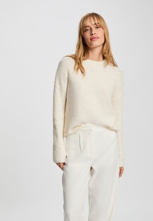 Suéter de textura color crema, con mangas largas y cuello redondo, combinado con pantalones a medida de color claro.