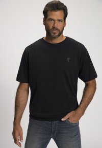 T-shirt nera a maniche corte realizzata in tessuto morbido, con un piccolo logo discreto sul petto. Accoppiata con jeans blu strappati.