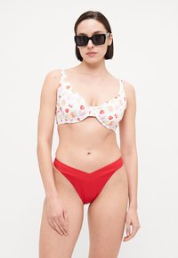 Zweiteiliges Bikini-Set mit einem weißen, blumenbedruckten Bralette mit roten Akzenten und einem passenden, hochgeschnittenen roten Höschen mit V-Form.