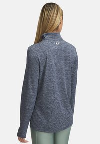 Dunkelblauer Langarmpullover mit hohem Kragen, strukturiertem Stoff und kleinem Logo auf der Rückseite des Halses. Möglicherweise aus feuchtigkeitsableitendem Material gefertigt.