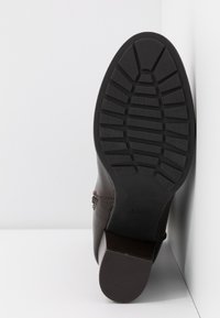 Bota de cuero marrón con suela de goma negra estriada, que muestra patrones texturizados y un tacón bajo. Características laterales con costuras decorativas.