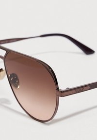 Καφέ μεταλλικά γυαλιά ηλίου με βαθμιαίους φακούς, με κομψό σχέδιο πλαισίου και «QUAY» χαραγμένο στο μπράτσο. Ομαλή υφή και ελάχιστες λεπτομέρειες.