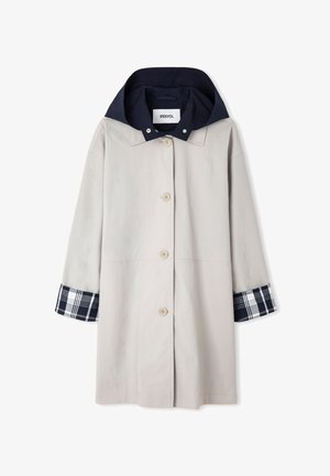 Manteau long beige clair avec boutons sur le devant, capuche bleu marine et poignets à motif écossais bleu marine et blanc.