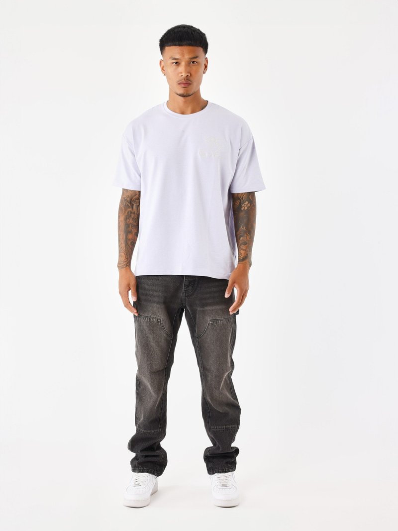 Camiseta blanca de manga corta con un pequeño logo en el pecho, combinada con unos vaqueros negros desgastados y zapatillas blancas.