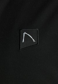 Zwarte stofpatch met een minimalistisch wit logo ontwerp. De patch is rechthoekig met strakke lijnen en bestaat uit geborduurde details.