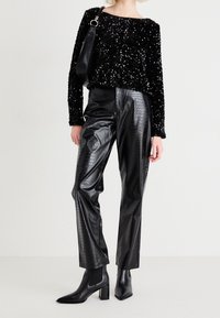 Haut en sequins noirs à manches longues, associé à un pantalon noir en simili cuir taille haute présentant un motif crocodile et des bottines à bout pointu.
