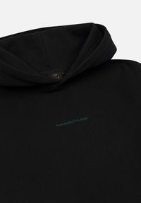 Zwarte hoodie met kleine teal "TOMORROWLAND" tekst gecentreerd op de borst, plat gelegd tegen een witte achtergrond.