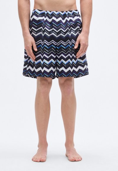 Costume da bagno con motivo a zigzag blu, nero e bianco. Realizzato in tessuto liscio e leggero con una cintura elastica.