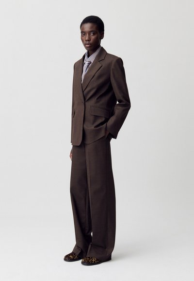 Completo marrone su misura con un blazer strutturato e pantaloni a gamba larga. Include una camicia a righe leggere e calzature con stampa animale.
