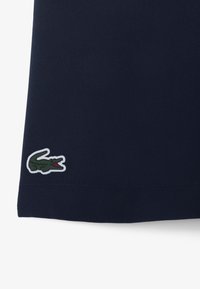 Polo azul marino con una textura suave, con un logo de cocodrilo bordado en verde en el dobladillo, acentuado por detalles en blanco.