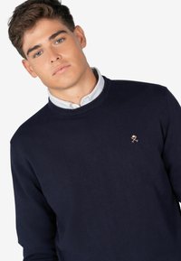 Maglione a collo rotondo di colore blu navy, realizzato in tessuto a maglia, con un piccolo ricamo del logo sul petto.