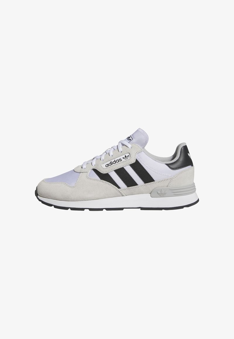 Adidas edzőcipők világosszürke velúrból és hálós anyagból, fekete csíkokkal, fehér talppal, fűzős dizájnnal és logós díszítésekkel a nyelvén és a sarkán.