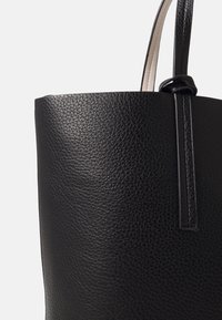 Czarna skórzana torba na ramię z teksturowaną powierzchnią, charakteryzująca się eleganckim designem i węzłowym zapięciem. Bocznie akcenty z kontrastowego gładkiego materiału.