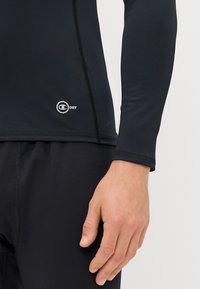 Hosszú ujjú fekete rash guard sima, rugalmas anyagból. Lapos varratokkal és logóval a bal szegélyen. Testhez simuló fazon.