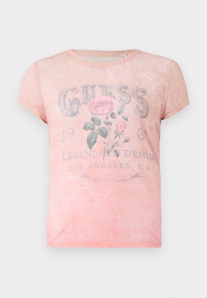 Roosa lühikeste varrukatega T-särk, millel on pleekinud lillemuster ja tekst "GUESS 1981 Legendaarne Denim Los Angeles, CA" ees.