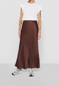 Gonna maxi in satin marrone abbinata a una t-shirt bianca a maniche corte e sneakers grigi, con una texture liscia e una silhouette snella.