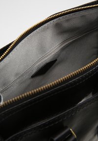 Intérieur d'un sac en cuir noir à la texture lisse, équipé d'une poche zippée et d'une doublure grise contrastante avec des détails de couture subtils.