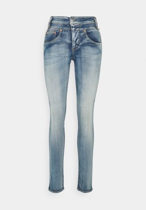 Jean skinny bleu délavé avec fermeture à boutons sur le devant et cinq poches, présenté sur fond blanc.